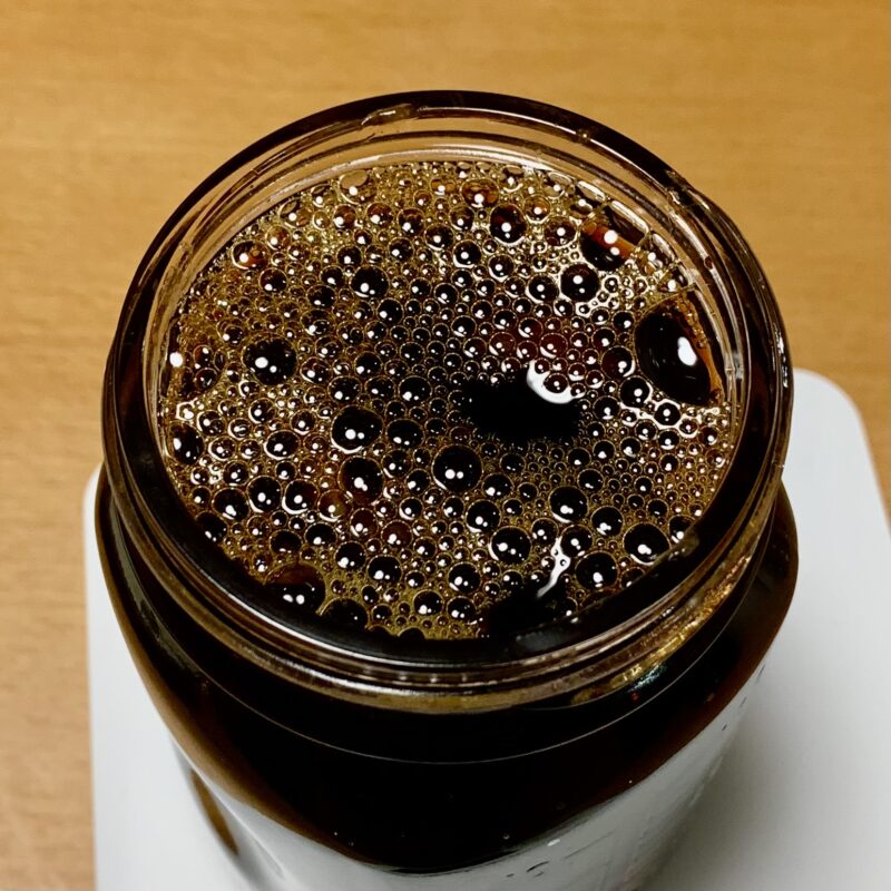 保存瓶の中に梅の種を入れ、そこに醤油を注ぎ入れた直後の様子。これからじっくりと梅醤油を漬け込む工程。 瓶の中で醤油と梅の種が馴染み、表面に細かな泡が浮いている様子。漬け込み中の梅醤油。